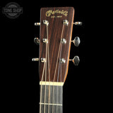 Close-up of the headstock of a Martin & Co acoustic guitar against a black background, showing the dark wood grain, gold script logo, and six silver tuning pegs. A Tone Shop watermark is visible in the top-left corner.