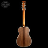 The back of an acoustic guitar with a dark brown wood grain finish, shown against a solid black background. A Tone Shop watermark is visible in the top-left corner.