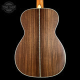 The back of an acoustic guitar with a rich dark brown wood grain finish, featuring a single light-colored center stripe and white edge binding, shown against a solid black background with a Tone Shop watermark in the top left.