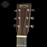 Close-up of the headstock of a Martin & Co acoustic guitar against a black background, showing the brand name in gold script, six tuning pegs, and part of the dark wood neck.