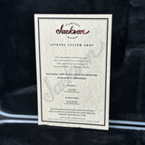 A white paper certificate card from Jackson Custom Shop with printed text and a decorative border, placed on a dark plush fabric background.