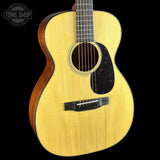 An acoustic guitar with a natural wood finish and a dark tortoiseshell pickguard, shown against a solid black background with a Tone Shop watermark in the top-left corner.