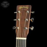 Close-up of a Martin & Co acoustic guitar headstock with six silver tuning pegs and strings, set against a solid black background.