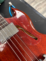 Close-up of a red electric bass guitar with a black case in the background