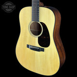 A close-up studio shot of an acoustic guitar body against a black background, showing a natural wood grain top, dark pickguard, black bridge, and part of the dark wood sides. A Tone Shop logo watermark is visible in the upper left corner.