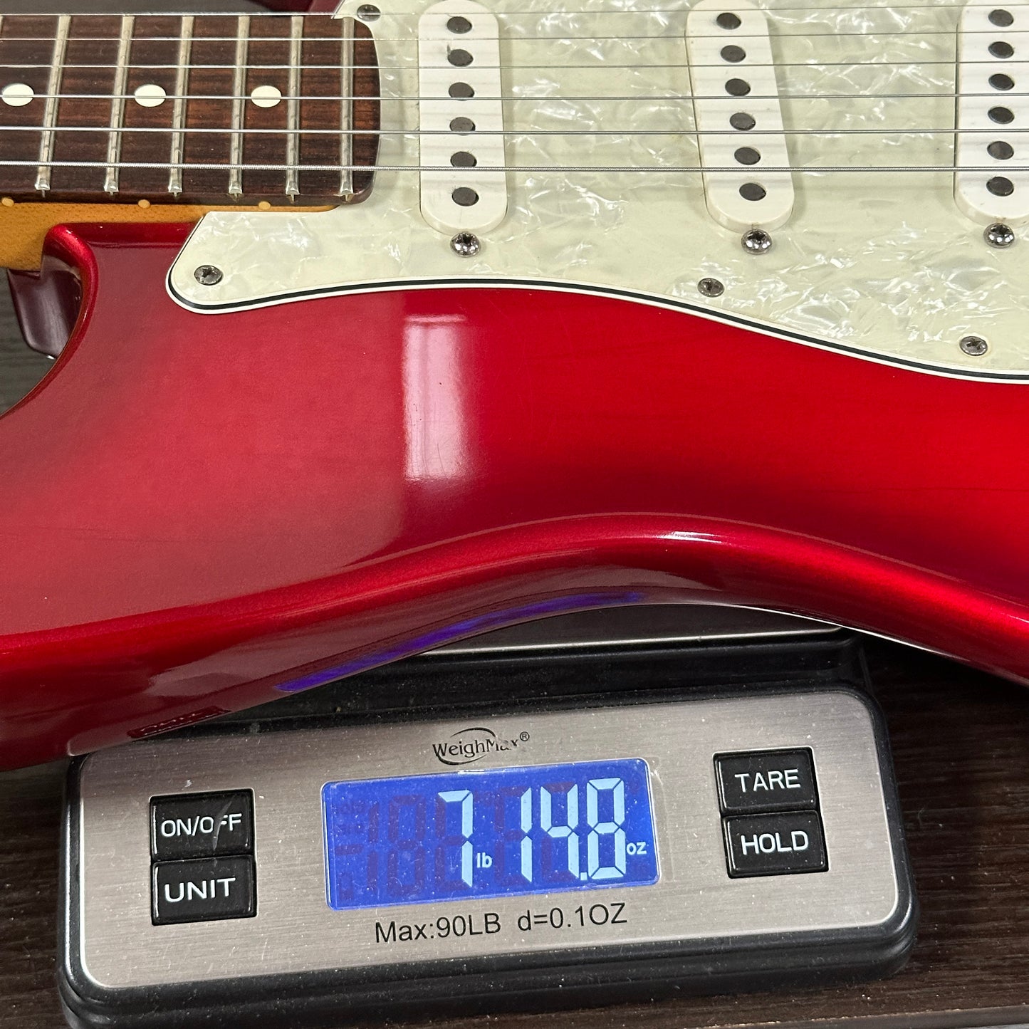 Red electric guitar on a digital scale displaying weight