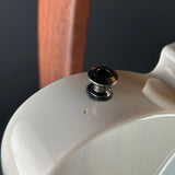 Close-up of a glossy off-white ceramic or porcelain surface with a small black and silver metal cap or plug on top, against a dark background with a blurred wooden vertical element.