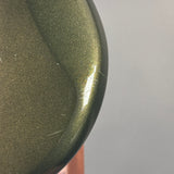 Close-up of a metallic olive green curved surface with a glossy finish and fine glitter texture, against a plain light gray background.