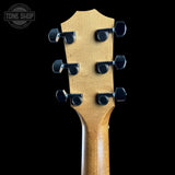 Close-up of the headstock of a guitar, showing six black tuning pegs and a natural wood grain finish, set against a solid black background with a Tone Shop watermark in the top left corner.