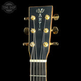 Close-up of a guitar headstock with gold-tone tuning pegs and a black face featuring the vertically printed 'G Martin' brand name, shown against a black background.
