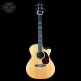 A natural wood acoustic-electric guitar with a cutaway body, dark fretboard, and dark pickguard, shown against a solid black background with a Tone Shop watermark in the top-left corner.