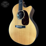 A close-up of a Taylor acoustic guitar against a solid black background, featuring a natural wood finish, a dark tortoiseshell pickguard, and a black bridge. A 'TONE SHOP' watermark is visible in the top-left corner.