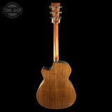 The back view of a wooden acoustic guitar with a cutaway body and six-string tuning system, shown against a solid black background with a Tone Shop watermark in the top-left corner.