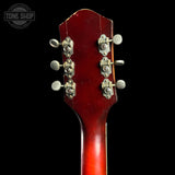 Close-up of the headstock of a vintage acoustic guitar, showing six silver tuning pegs and a glossy red-finish top against a black background.