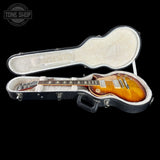 A sunburst electric guitar inside an open black hard case with a cream-colored padded interior, shown against a solid black background. A Tone Shop watermark is visible in the top-left corner.