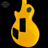 The back of a bright yellow electric guitar, showing the glossy finish, black pickguard, and circular gold-toned hardware against a solid black background.