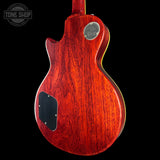 The back of a Gibson Les Paul Custom electric guitar with a glossy reddish-brown cherry wood finish, featuring a chrome 'Gibson Les Paul Custom' emblem and a black pickguard, shown against a solid black background.