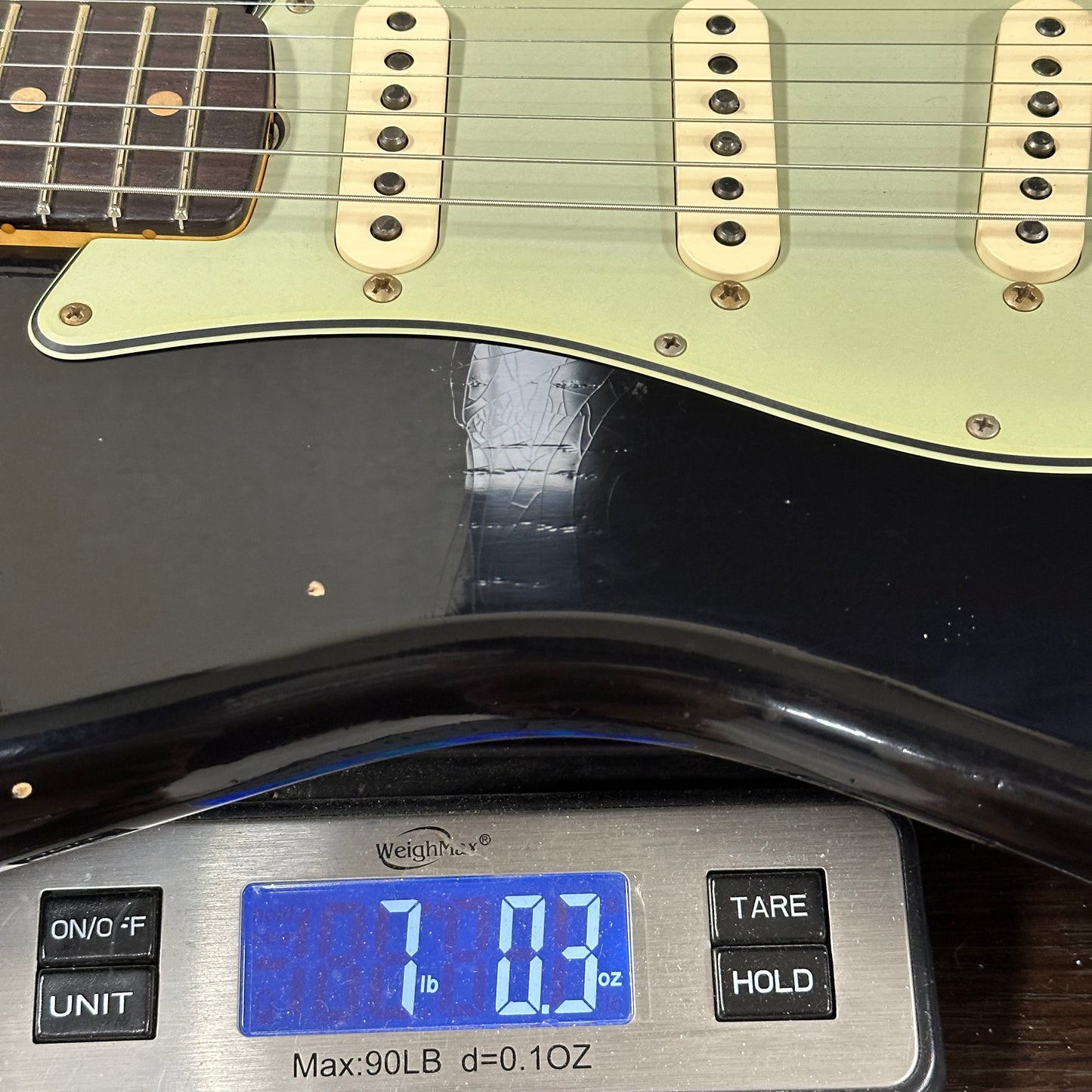 Light green electric guitar on a digital scale displaying weight.