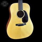 A close-up studio shot of an acoustic guitar body against a solid black background, featuring a natural wood grain top, dark sides, and a black pickguard. A Tone Shop watermark is visible in the upper left corner.