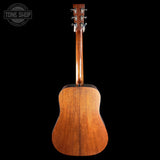 The back of a wooden acoustic guitar, showing the rich grain and finish of the mahogany body and neck, photographed against a solid black background with a Tone Shop watermark in the top left corner.