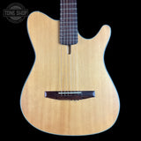 A close-up of a wooden electric guitar body with a natural light wood finish, dark brown bridge and headstock area, and a black background. A Tone Shop watermark is visible in the top left corner.