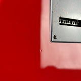 Close-up detail of a red metal surface with a black rectangular panel, screw, and small vent-like opening.