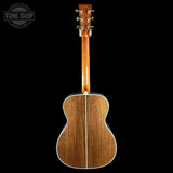 The back of an acoustic guitar with a glossy brown wood finish and white binding, shown against a solid black background with a Tone Shop watermark in the top left corner.