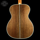 Close-up of the back of an acoustic guitar showing the wood grain on the backplate, with a white binding edge and a light wood neck visible at the top, set against a solid black background.