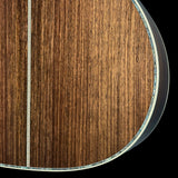 Close-up detail of an acoustic guitar's wooden body, showing the rich brown wood grain, a central sound hole rosette, and the edge of the instrument against a black background.