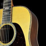 Close-up of an acoustic guitar body showing the natural wood top, dark brown sides, sound hole rosette, and black fretboard against a black background.