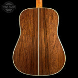 The back of an acoustic guitar made of rich, warm brown wood with a central seam and a light-colored edge binding, shown against a solid black background with a Tone Shop watermark in the top left.