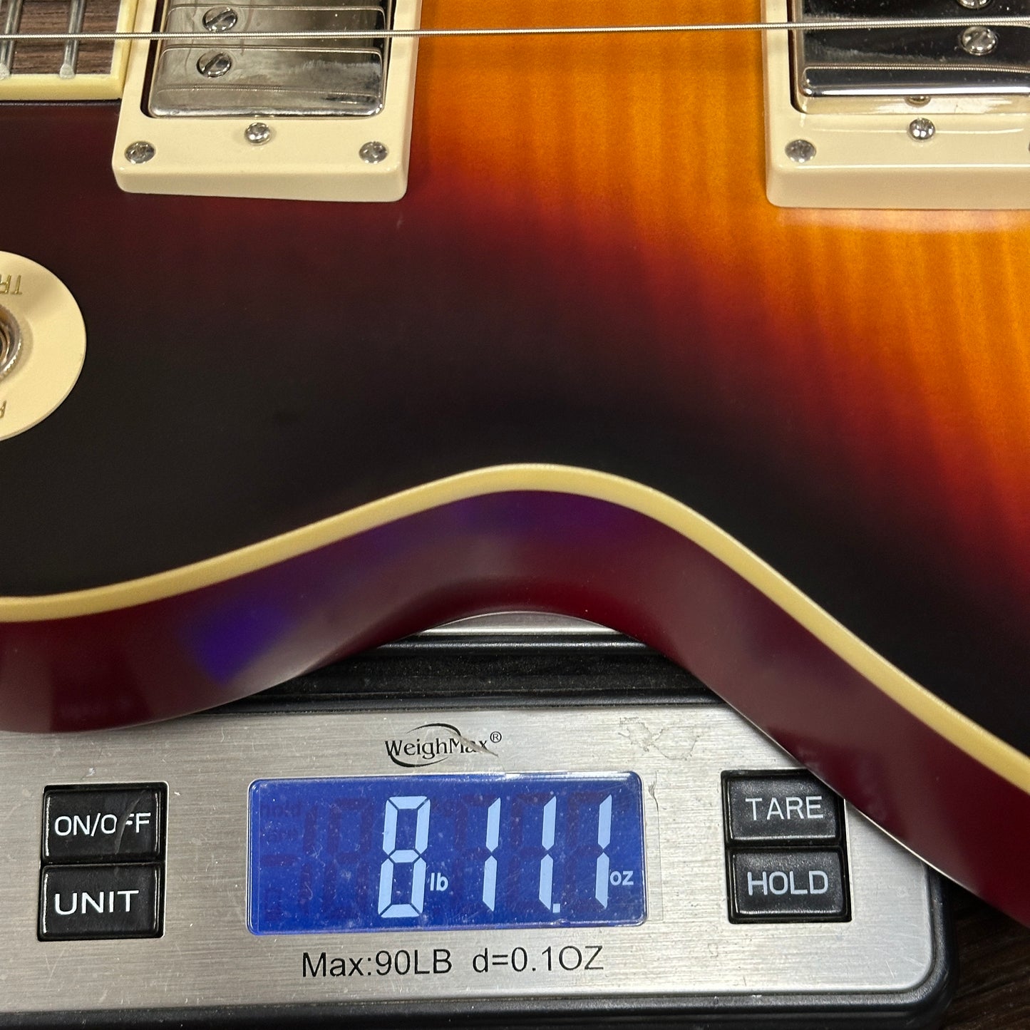 Guitar being weighed on a digital scale with a display showing weight.