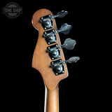 Close-up of the headstock of a bass guitar with four black tuning machines and silver tuning keys, set against a solid black background. A Tone Shop watermark is visible in the top left corner.