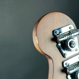 Close-up detail of a guitar headstock corner showing the brown wood finish and silver metal tuning pegs against a dark gray background.