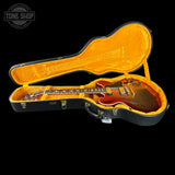 A sunburst electric guitar inside an open black hard case with a bright orange-yellow velvet lining, shown against a black background. A Tone Shop watermark is visible in the top-left corner.