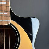 Close-up of an acoustic guitar body showing the glossy black pickguard, natural wood soundboard, and part of the fretboard against a dark gray background.