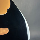 Close-up of a glossy black guitar body with a curved edge and light wood inlay, photographed against a dark gray background.