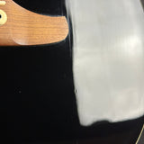 Close-up of a glossy black guitar body with a light gray reflective patch on the right side and part of a brown wood neck visible at the top left.