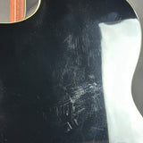 Close-up of a glossy black guitar body with visible scratches and scuffs on the back, plus a white light reflection on the right side.
