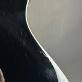 Close-up of a glossy black electric guitar body with a white binding edge against a neutral gray background.