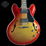 A double-cutaway electric guitar with a red-to-gold sunburst finish, black pickguard, and chrome hardware, shown against a solid black background with a Tone Shop watermark in the top-left corner.