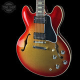 A double-cutaway electric guitar with a glittery red-to-gold sunburst finish, black pickguard, and chrome hardware, shown against a solid black background with a Tone Shop watermark in the top-left corner.