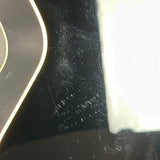 Close-up of a glossy black surface with visible scratches and dust, alongside a bright white area on the right and part of a curved gold-trimmed object on the left.