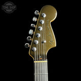 Close-up of a Fender electric guitar headstock in metallic gold with silver tuning pegs, shown against a solid black background. A Tone Shop watermark is visible in the top-left corner.