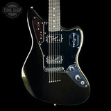 A black electric guitar with chrome hardware and a dark pickguard, shown from a front-three-quarter angle against a black background. A Tone Shop watermark is visible in the top-left corner.