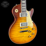 A classic electric guitar with a flamed sunburst finish, featuring a cream pickguard, chrome hardware, and gold-toned controls, shown against a solid black background.