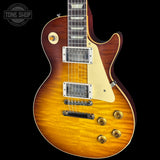 A Gibson Les Paul Custom electric guitar with a natural flame maple top, featuring a sunburst finish that transitions from bright yellow-orange to dark reddish-brown. It has a cream pickguard, chrome hardware, and gold-toned control knobs, shown against a solid black background with a Tone Shop watermark in the top left corner.