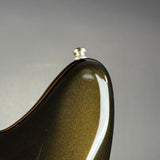 Close-up of the upper bout corner of a glossy electric guitar body, showing a metallic olive-gold finish with a silver hardware mount against a neutral gray background.