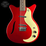 A red electric guitar with a cream-colored pickguard and maple top, shown against a solid black background. A Tone Shop watermark is visible in the upper left corner.