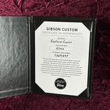 A Gibson Custom Certificate of Authenticity insert card displayed inside a black presentation folder on a textured burgundy velvet fabric background.